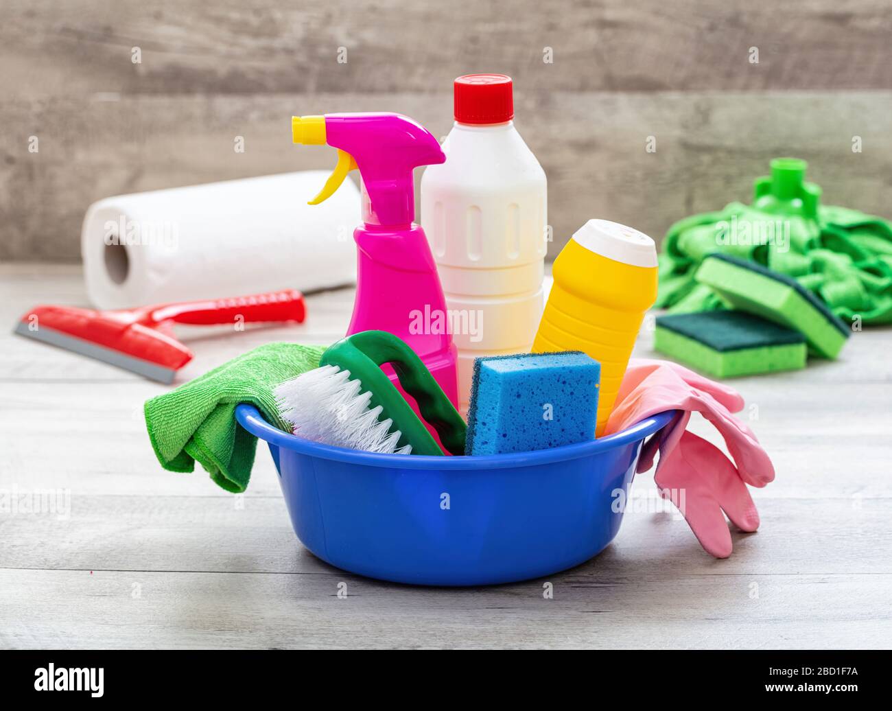 Prodotti per la pulizia sul pavimento, sfondo interno casa. Bottiglie di detergente chimico in un recipiente blu. Pulizia sanitaria domestica o aziendale Foto Stock