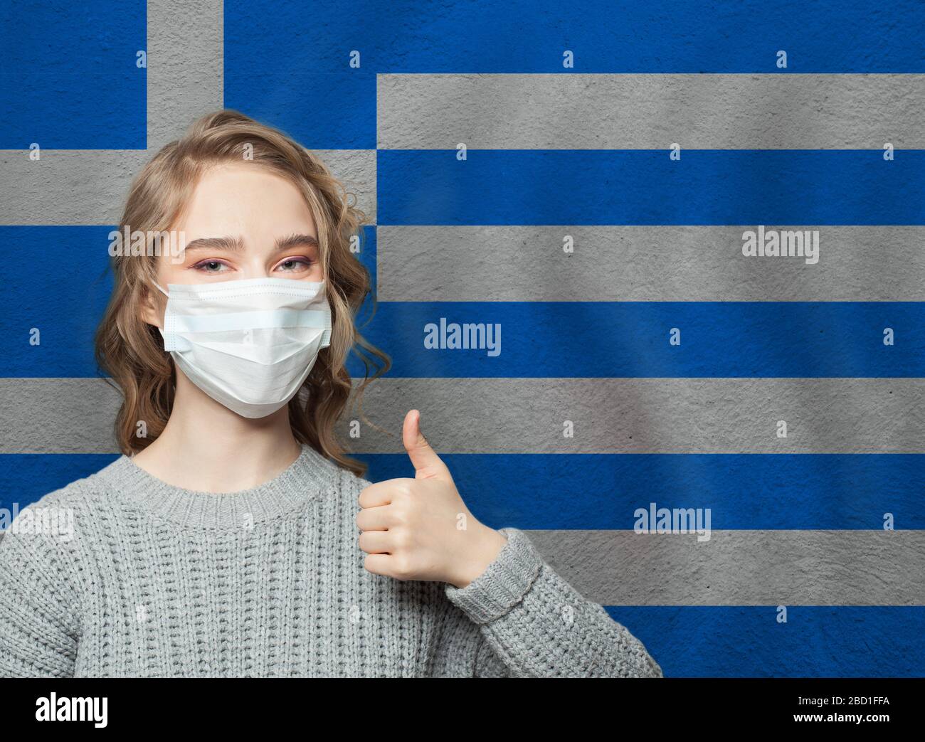 Donna felice in maschera viso tenendo il pollice in su sullo sfondo nazionale della bandiera greca. Concetto di protezione contro l'epidemia di influenza e i virus Foto Stock