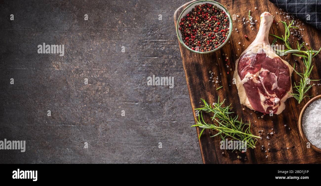 Vista dall'alto della preparazione della gamba d'anatra in un ambiente rustico scuro con tagliere in legno con ingredienti e condimenti che coprono la metà del quadro wi Foto Stock