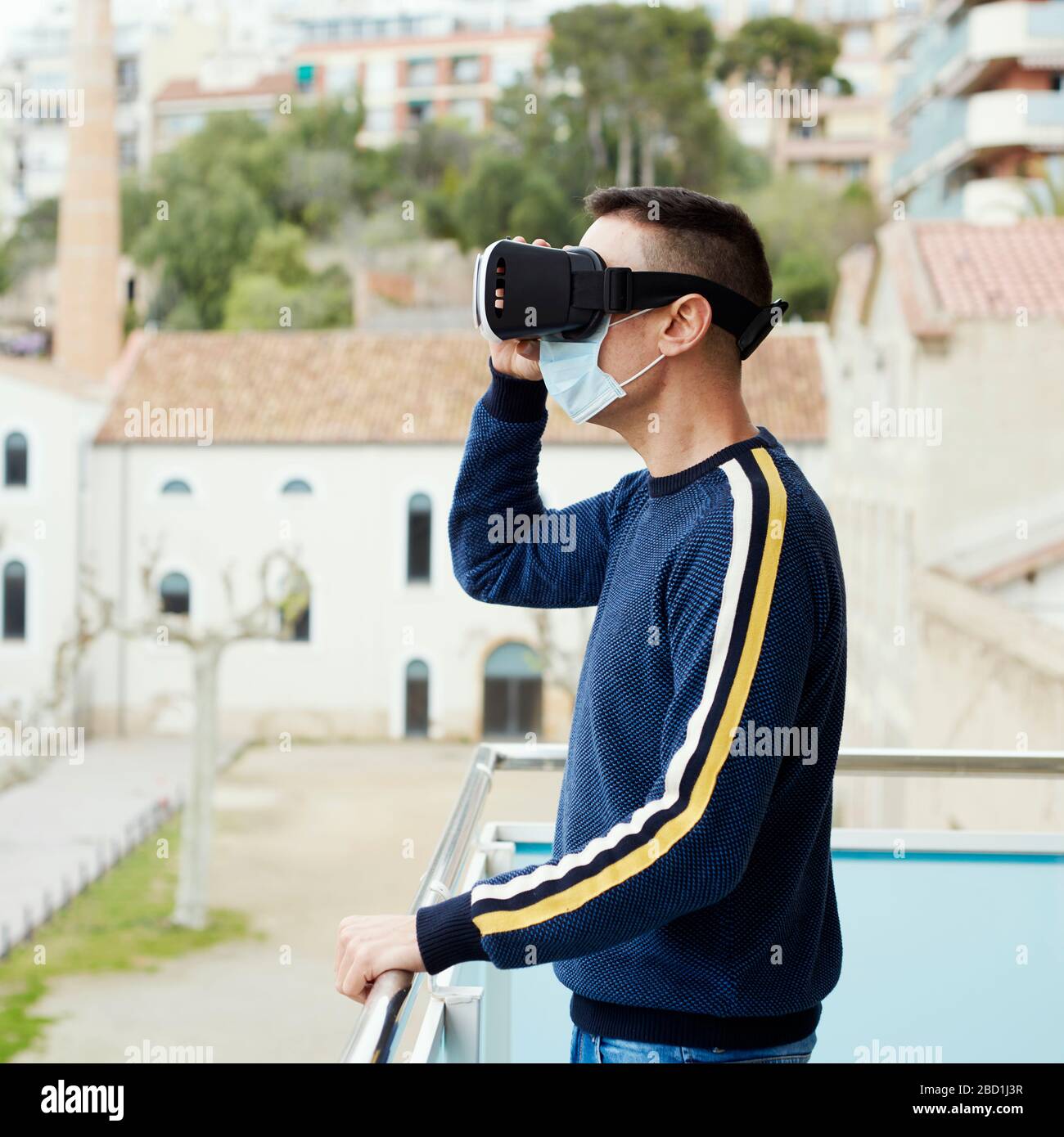 primo piano di un uomo caucasico, indossando una maschera chirurgica, utilizzando una cuffia per realtà virtuale in un balcone Foto Stock