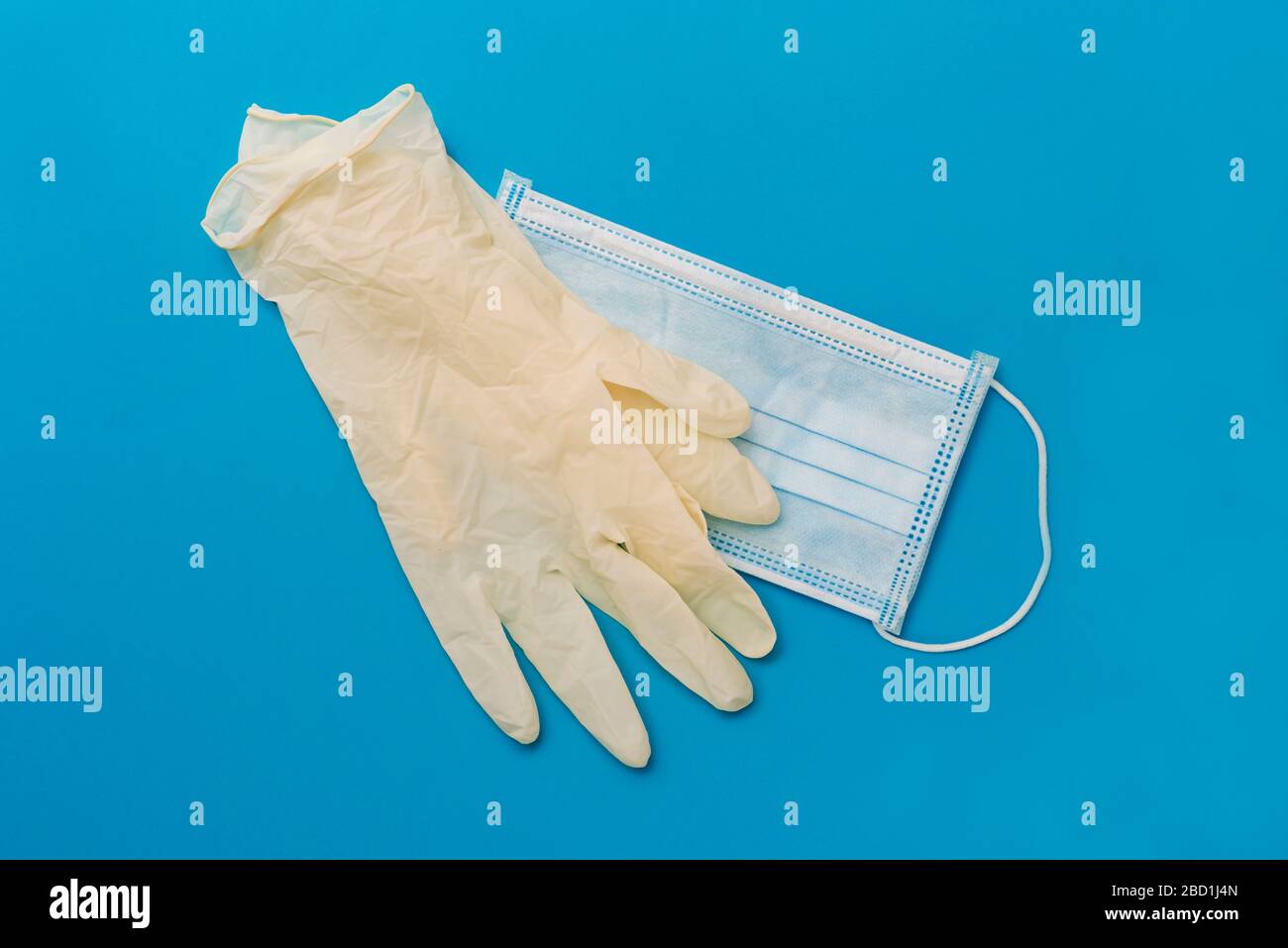 vista ad angolo elevato di un paio di guanti chirurgici monouso e di una maschera chirurgica monouso su sfondo blu Foto Stock