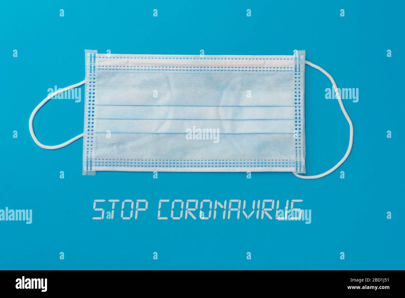 vista ad angolo elevato di una maschera chirurgica e il testo ferma coronavirus su uno sfondo blu Foto Stock