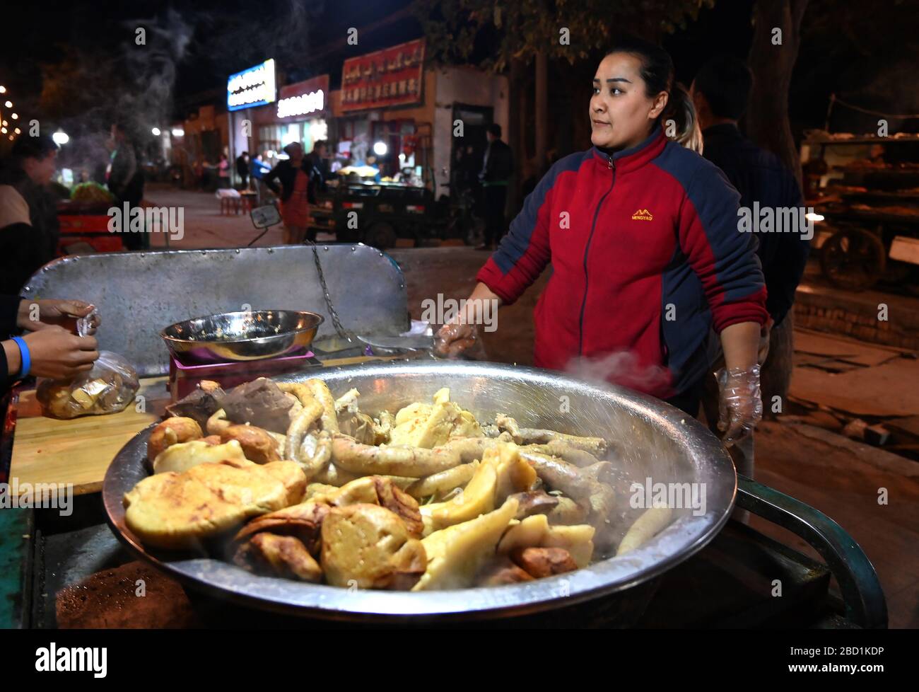 Donna che vende carni cotte da rickshaw stalla in Turfan notte mercato, Turfan, Xinjiang, Cina, Asia Foto Stock