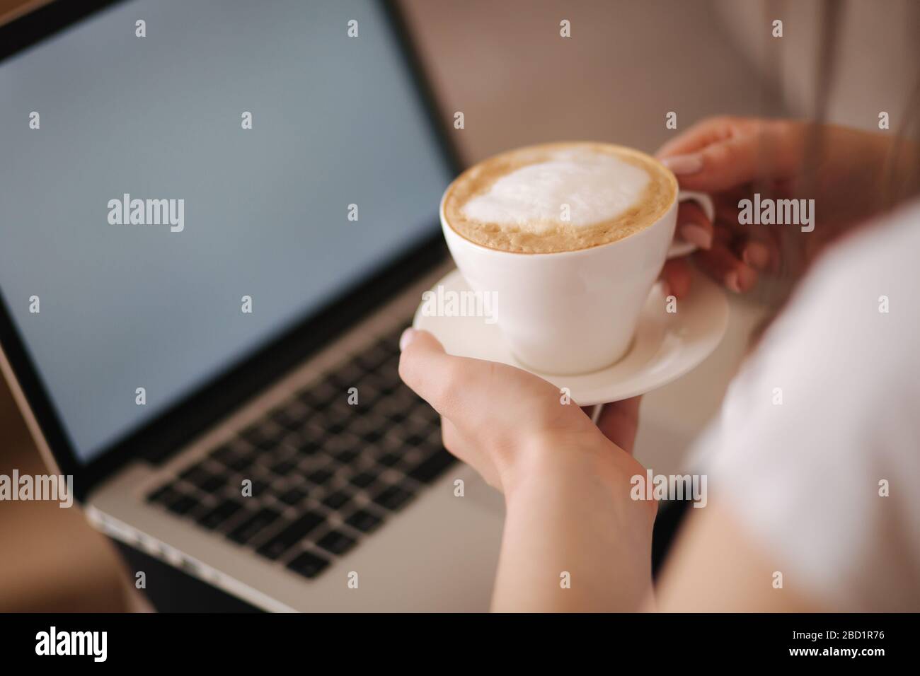 Vista in prima persona della donna che lavora a casa. Donna che lavora su un computer portatile e bere cappuccino. Scherma in bianco. Tempo di quarantena Foto Stock