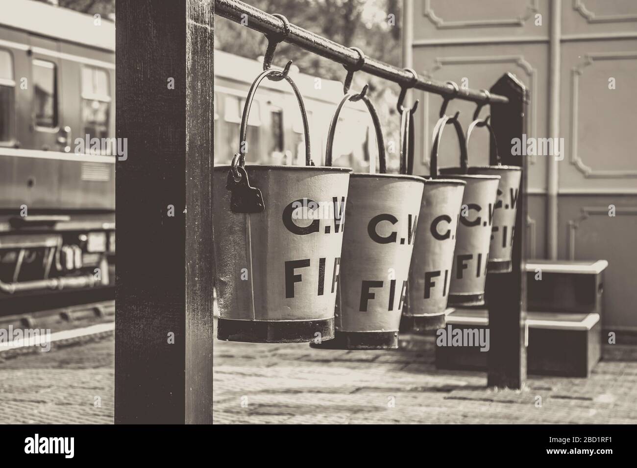Secchi del fuoco vintage in bianco e nero appesi in fila sulla piattaforma della stazione ferroviaria vintage, la ferrovia a vapore della Severn Valley. Vecchia attrezzatura antincendio. Foto Stock