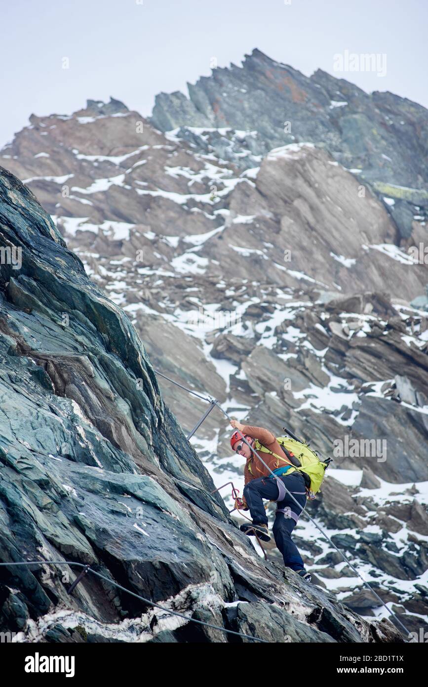 Alpinista con zaino con corda fissa per salire su alta montagna rocciosa. Uomo arrampicatore ascendente cresta alpina e cercando di raggiungere la cima della montagna. Concetto di alpinismo e arrampicata alpina. Foto Stock