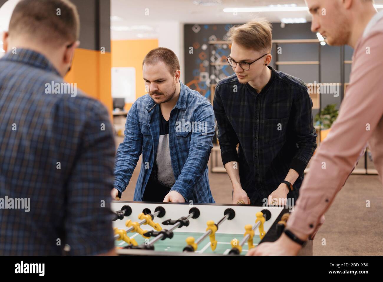 Gruppo di giovani lavoratori d'ufficio che giocano gioco di calcio da tavolo all'interno dell'ufficio durante il loro tempo di pausa. Foto Stock