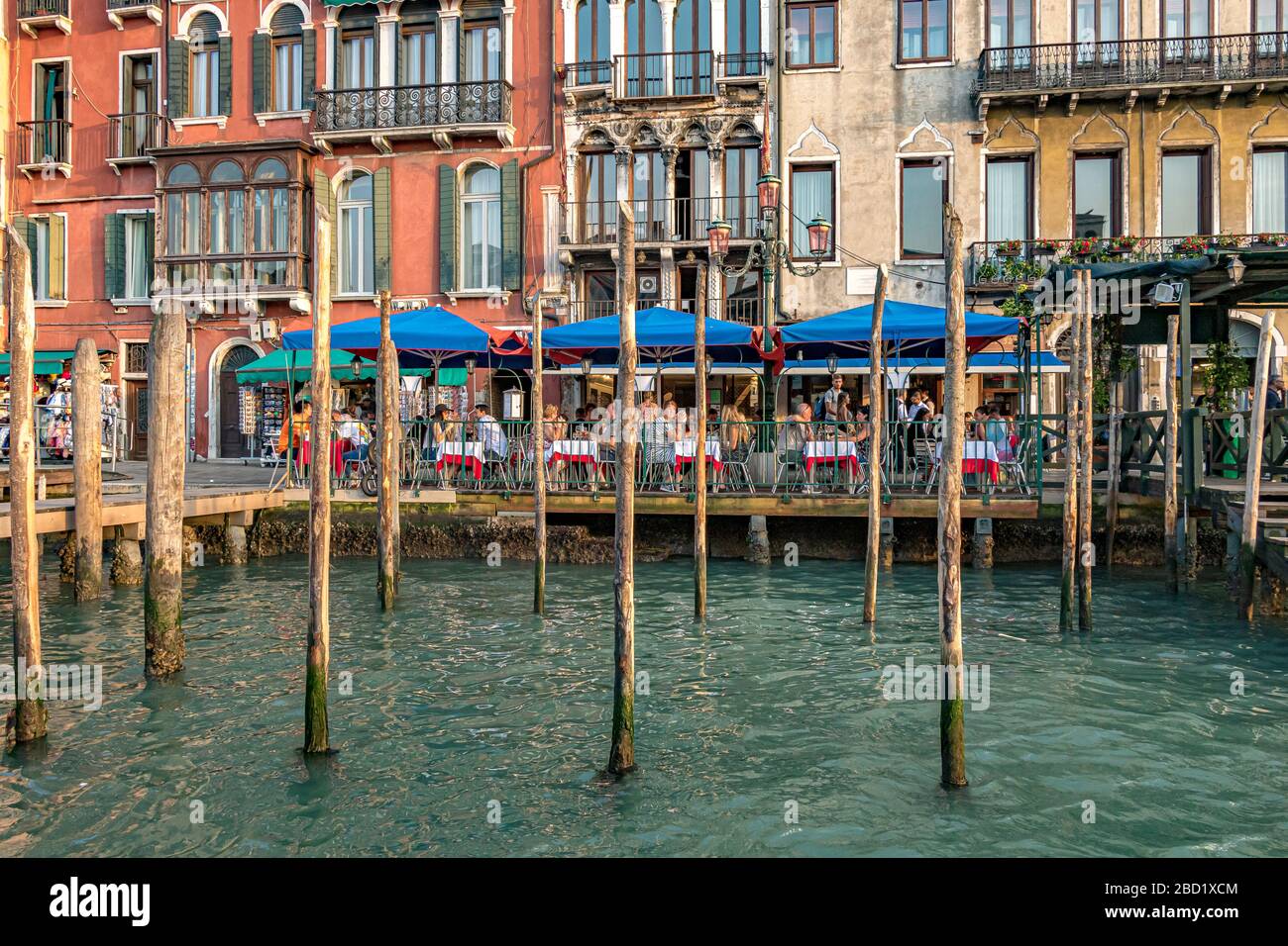 Per i pasti, si mangia all'aperto in un ristorante italiano di fronte ai pali in legno vicino a Rialto sul Canal Grande, Venezia, Italia Foto Stock
