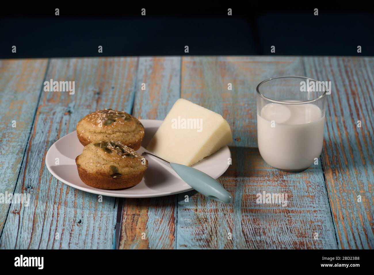 Pane di mais a forma di muffin ( proja ) con semi di sesamo e zucca con formaggio e bicchiere di yogurt. Cucina balcanica. Legno rustico blu Foto Stock