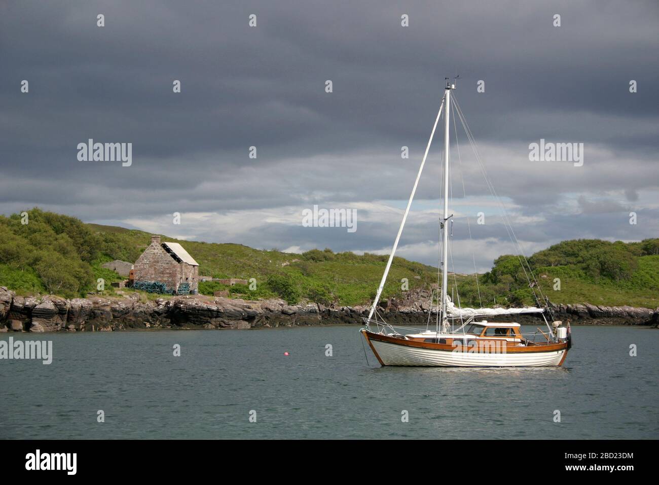 Barca a vela ancorata nel porto di Soay e le rovine della stazione di pesca degli squali di Gavin Maxwell, Soay, Isola di Skye, Ebridi, Scozia Foto Stock