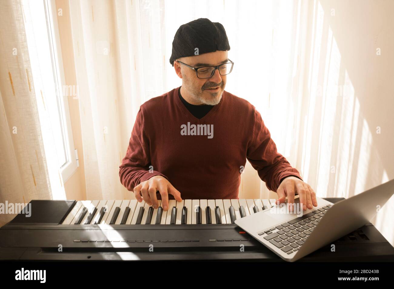 Un uomo che impara a suonare il pianoforte online con un computer che si trova a casa. Concetti di auto insegnato, rimanere a casa e lavorare online Foto Stock
