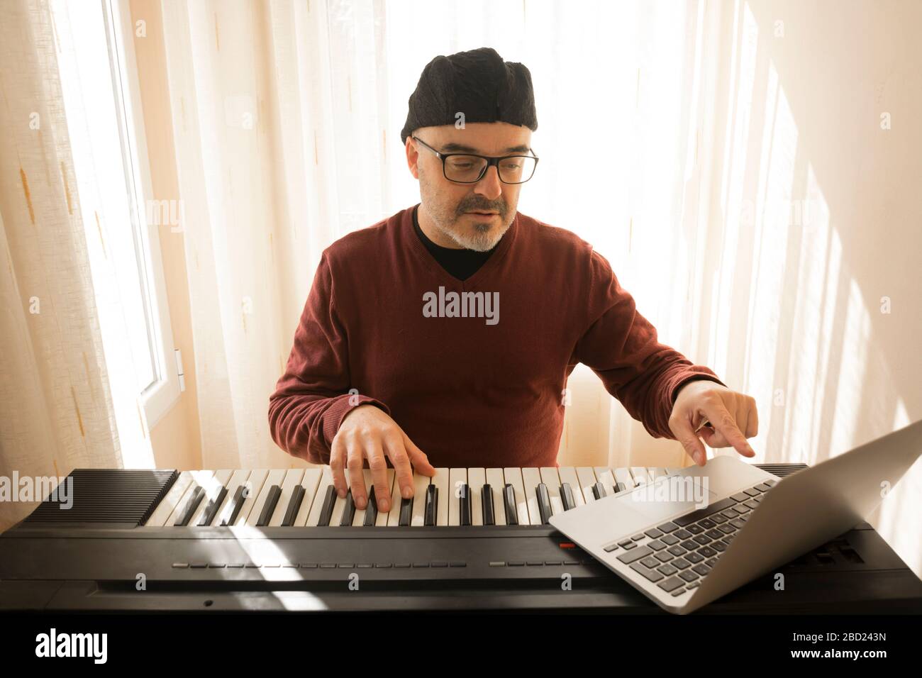 Un uomo che impara a suonare il pianoforte online con un computer che si trova a casa. Concetti di auto insegnato, rimanere a casa e lavorare online Foto Stock