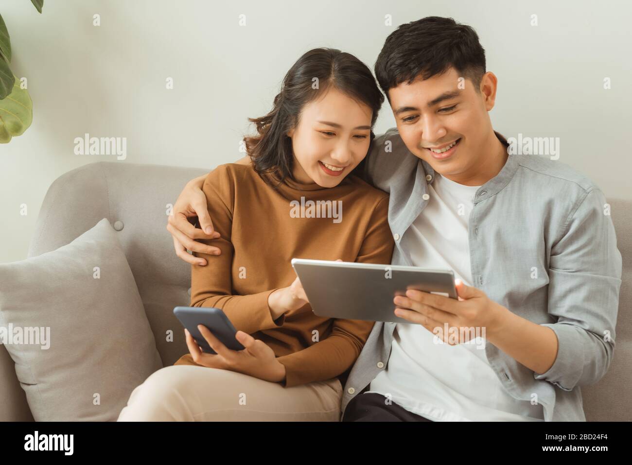 concetto di svago, tecnologia e dipendenza da internet: coppia felice con computer tablet e smartphone a casa Foto Stock