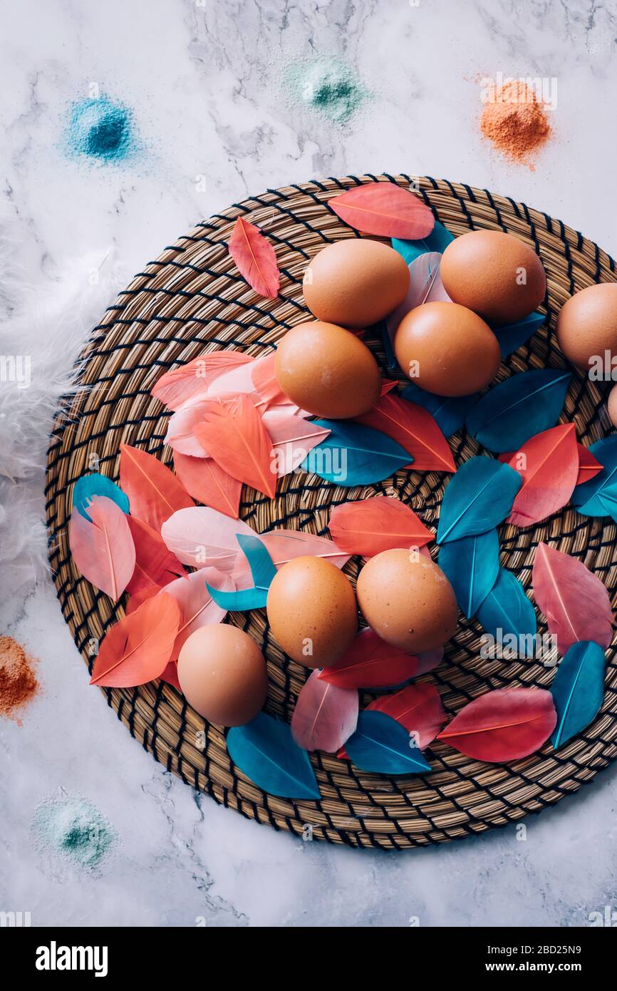 Colorata composizione pasquale delle uova di pollo, piume di uccelli colorate, tinture per le uova sul tavolo di marmo. Prepararsi per la festa di pasqua. Vista dall'alto Foto Stock