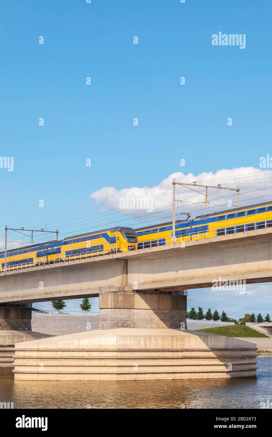 Treno olandese che attraversa le fiancate del fiume Waal di fronte alla città di Nijmegen, Paesi Bassi Foto Stock