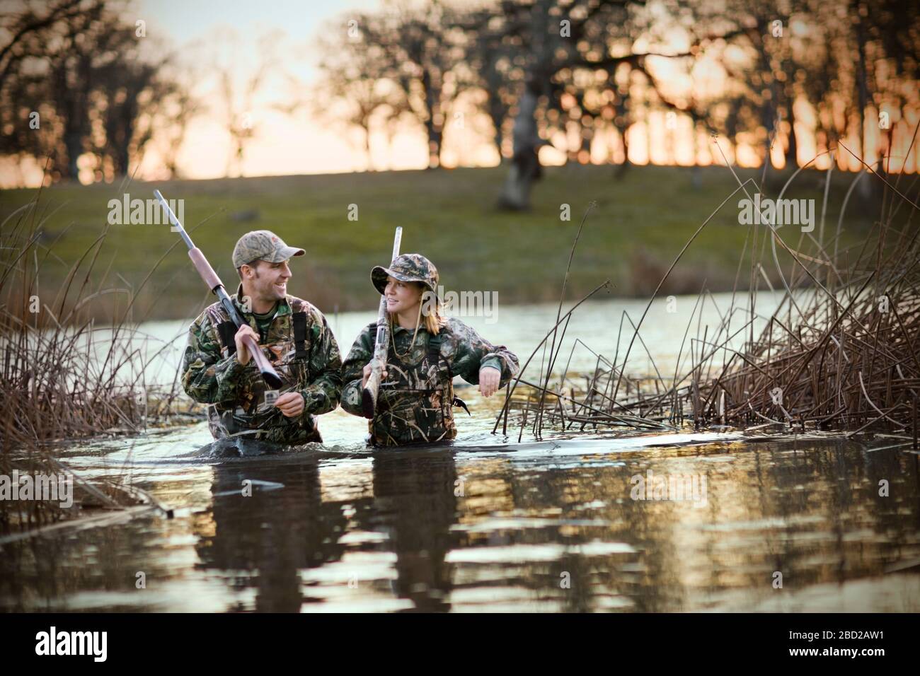 Cacciatore maschio e femmina che guadi attraverso un lago che trasporta i fucili Foto Stock