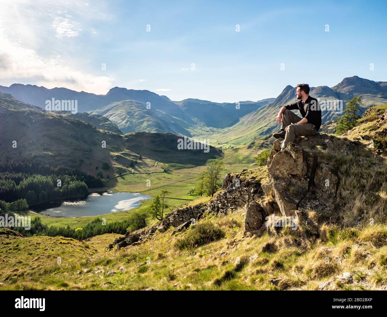 Un camminatore si riposa guardando Blea Tarn, un piccolo lago nel Distretto dei Laghi, Cumbria, Inghilterra. Foto Stock