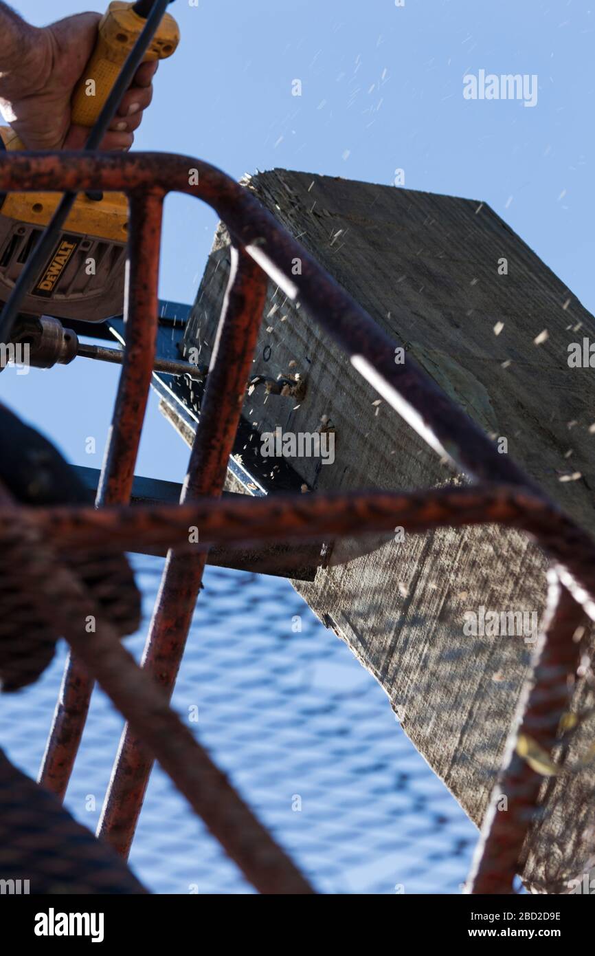 Una vista ravvicinata di un operatore edile che utilizza un trapano rotante e una punta per legno su un palo Foto Stock