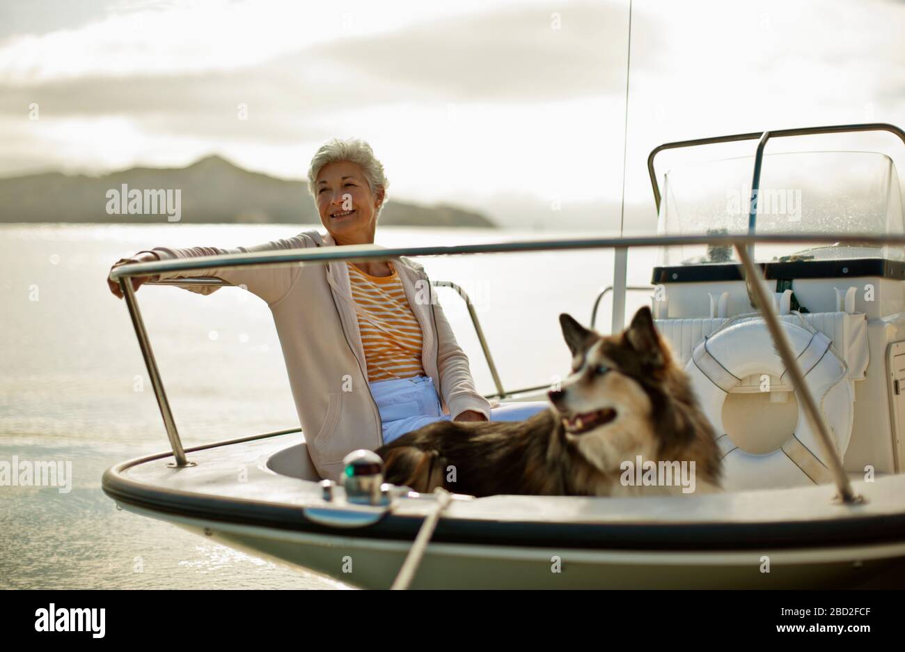 Sorridente donna matura si rilassa su una barca con i suoi grandi e soffici cane. Foto Stock