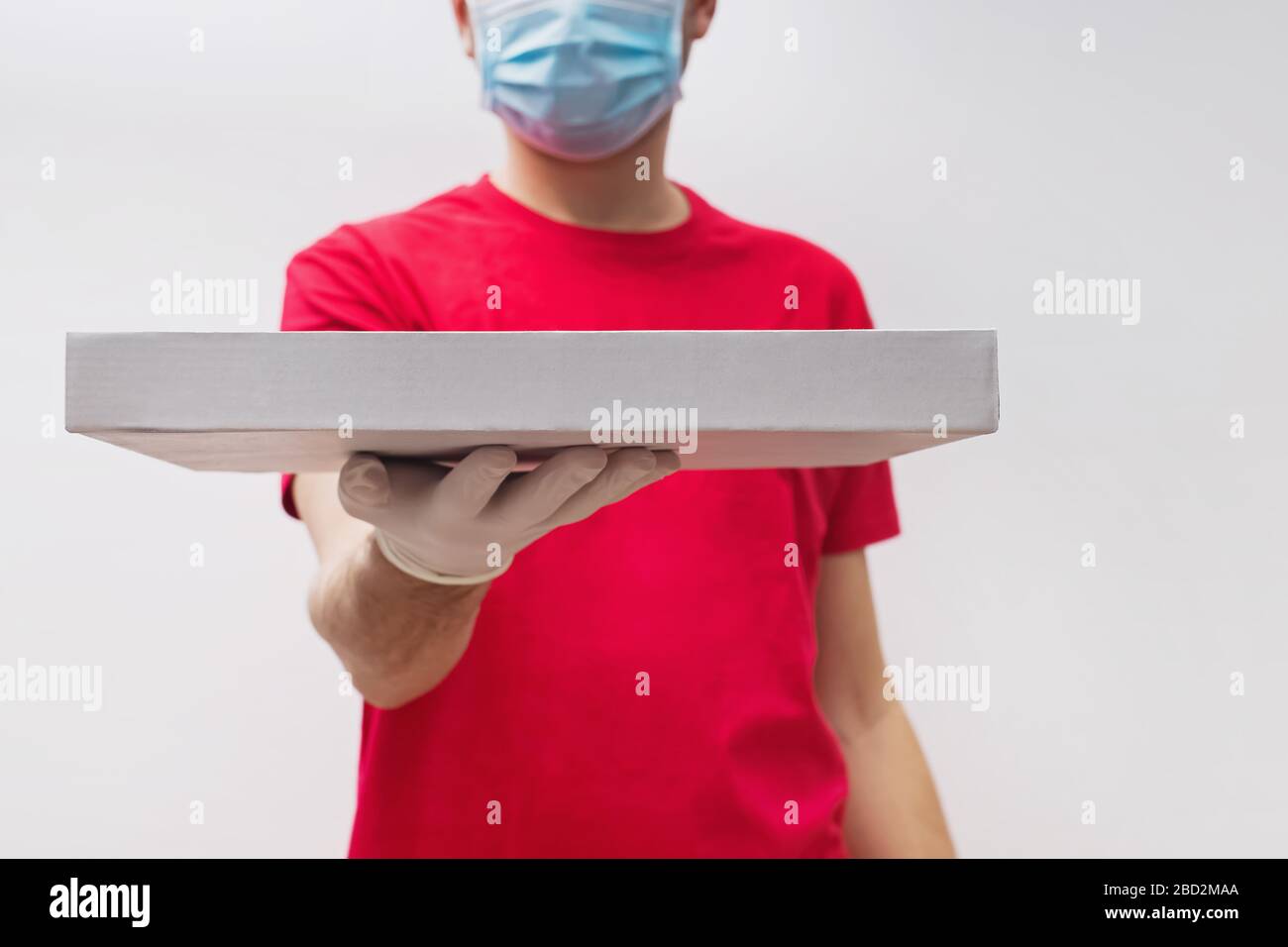 Uomo dal servizio di consegna in t-shirt rossa, indossando maschera protettiva e guanti dando scatola pizza. Foto Stock