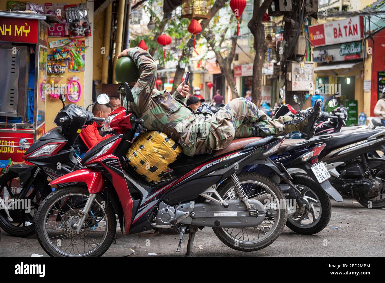 Un soldato si rilassa sul suo scooter ad Hanoi, Vietnam Foto Stock