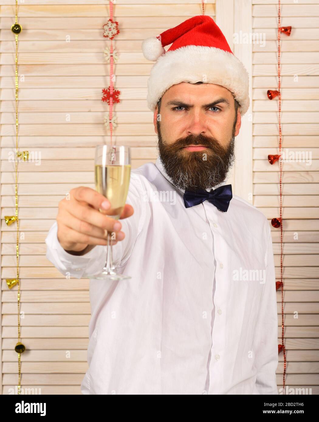 L'uomo con barba e cravatta a prua tiene un bicchiere di champagne. Ragazzo  su sfondo muro di legno con ghirlande rosse. Concetto di festa e di  allegrie. Babbo Natale in cappello rosso