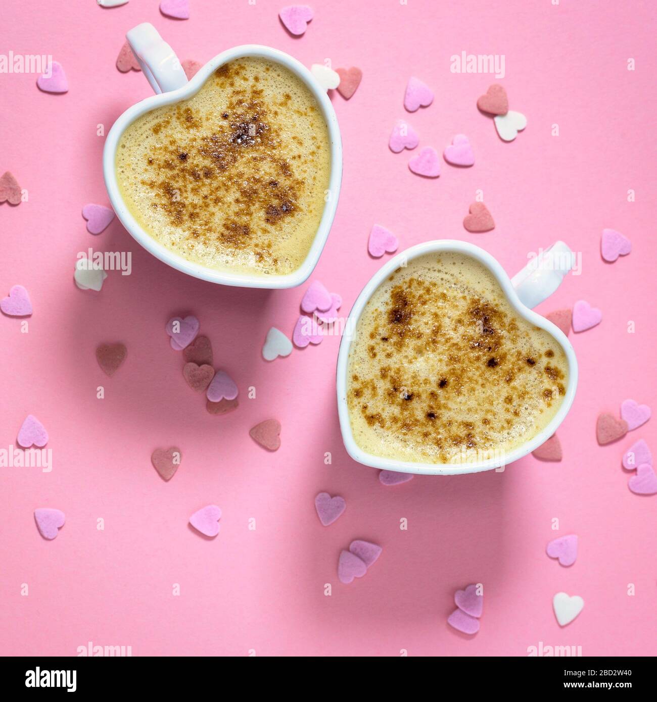 Due tazze da caffè a forma di cuore su sfondo rosa pastello, vista dall'alto con spazio per le copie. Concetto di amore. Foto Stock