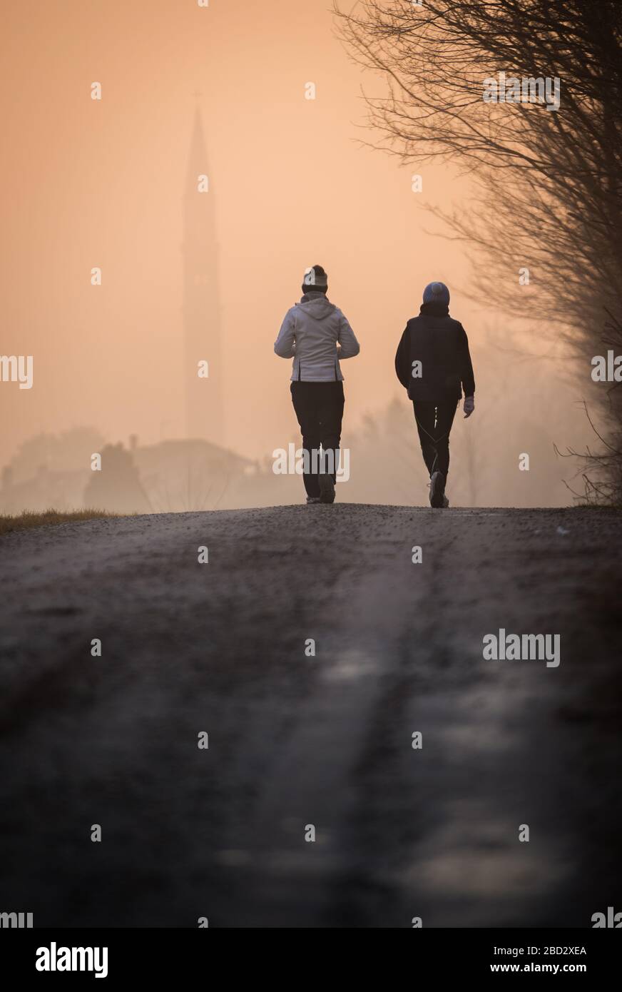 Primo piano di due ragazze che camminano giù una strada sterrata nella luce del mattino presto, con un villaggio lontano coperto di foschia Foto Stock