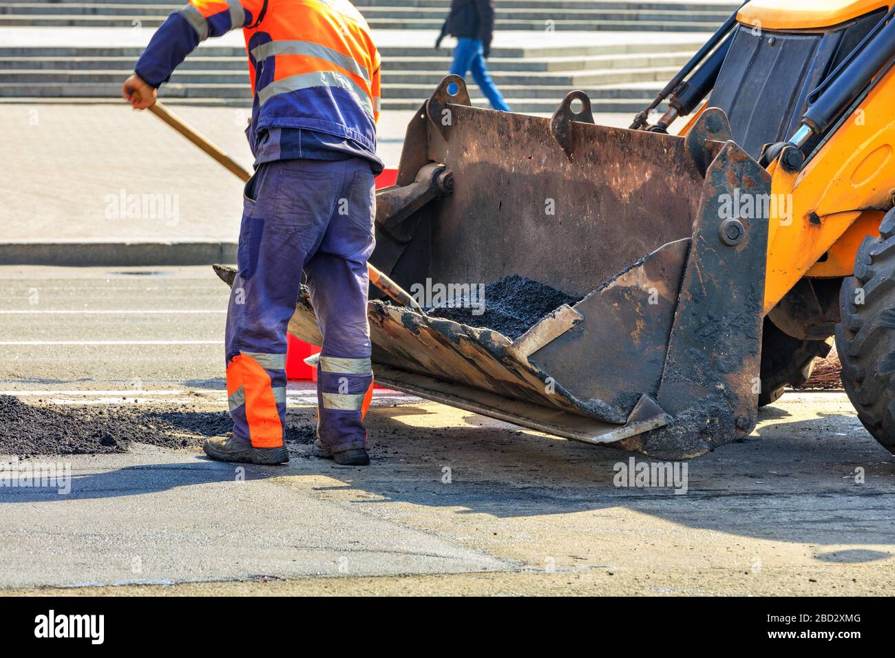 Un tecnico addetto alla manutenzione stradale versa asfalto fresco da una benna di un bulldozer durante la costruzione di strade. Foto Stock
