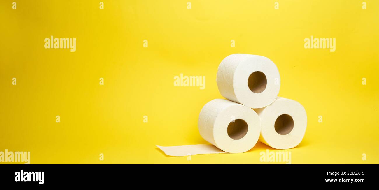 Ampio scatto di rotoli di carta igienica bianca su sfondo giallo minimalista Foto Stock