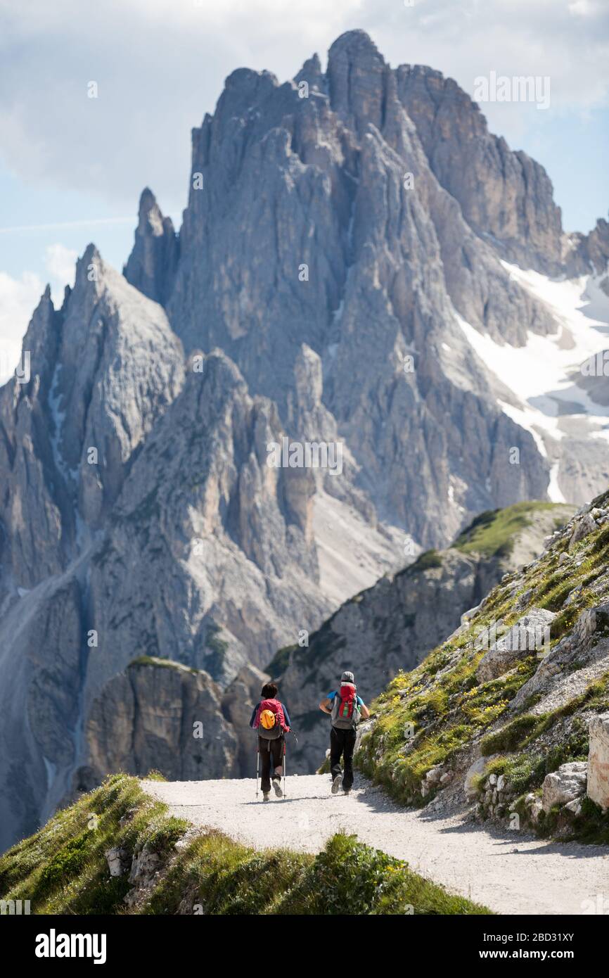 Un paio di escursionisti si trovano a piedi su una pista sterrata, con una montagna rocciosa sullo sfondo, in una soleggiata giornata estiva Foto Stock