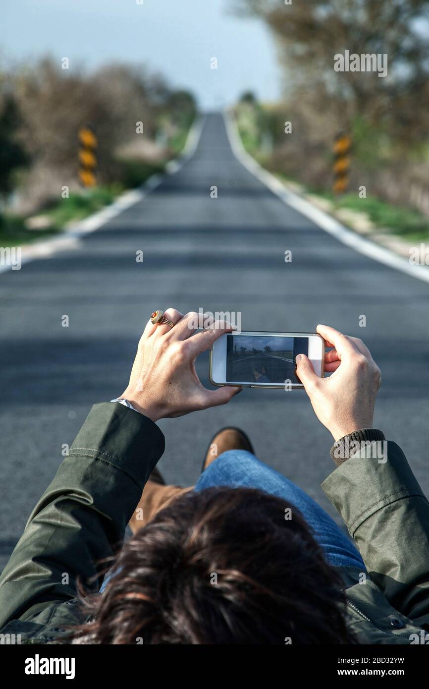 donna sdraiata a terra, in strada con il telefono cellulare in mano Foto Stock