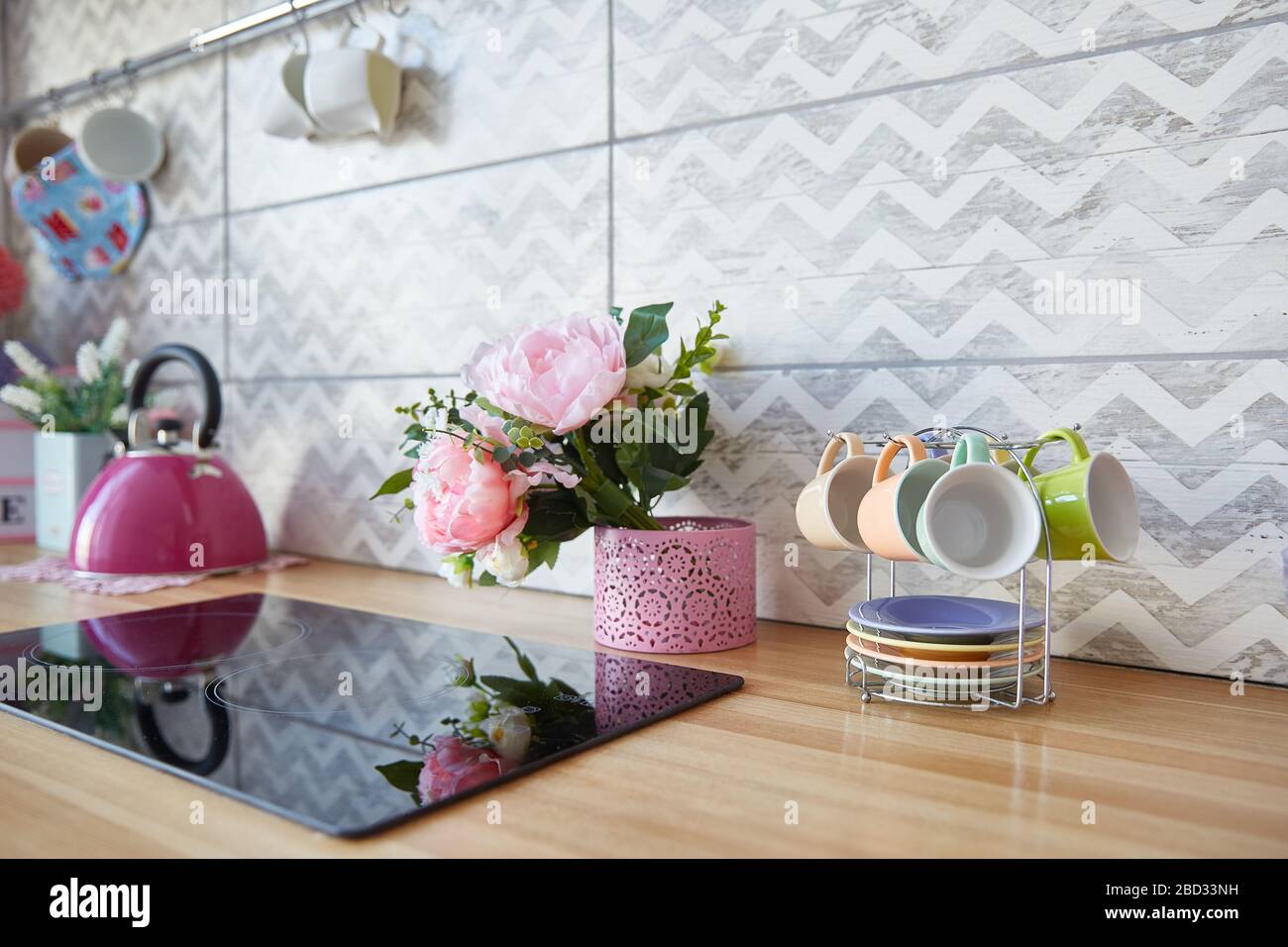 La superficie della cucina con un piano cottura nero. Fiori e tazze sul tavolo da cucina. Piano tavolo in legno all'interno della cucina. Foto Stock