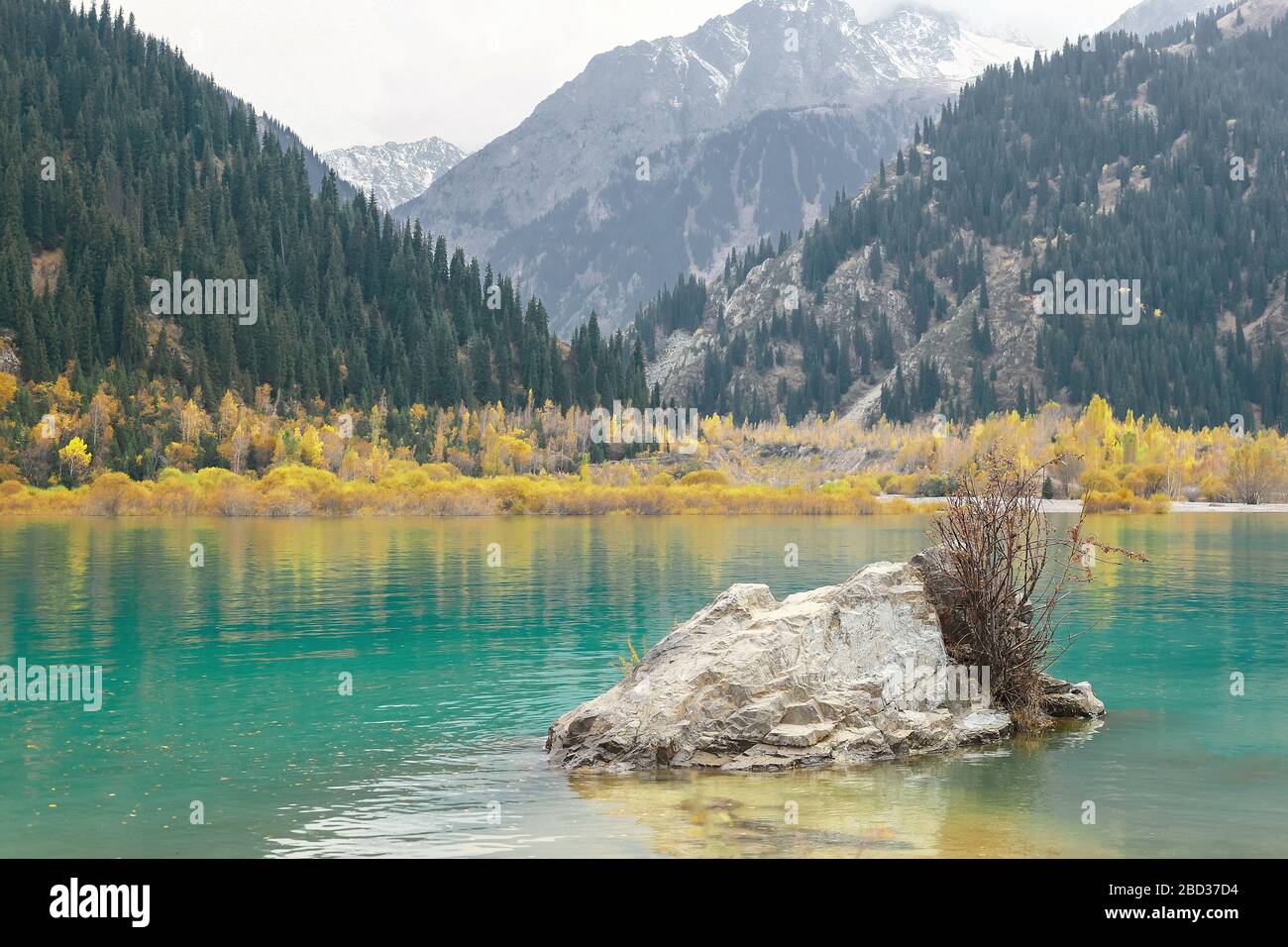 Una grande pietra in un lago di montagna sullo sfondo di un pendio fatiscente. Foto Stock