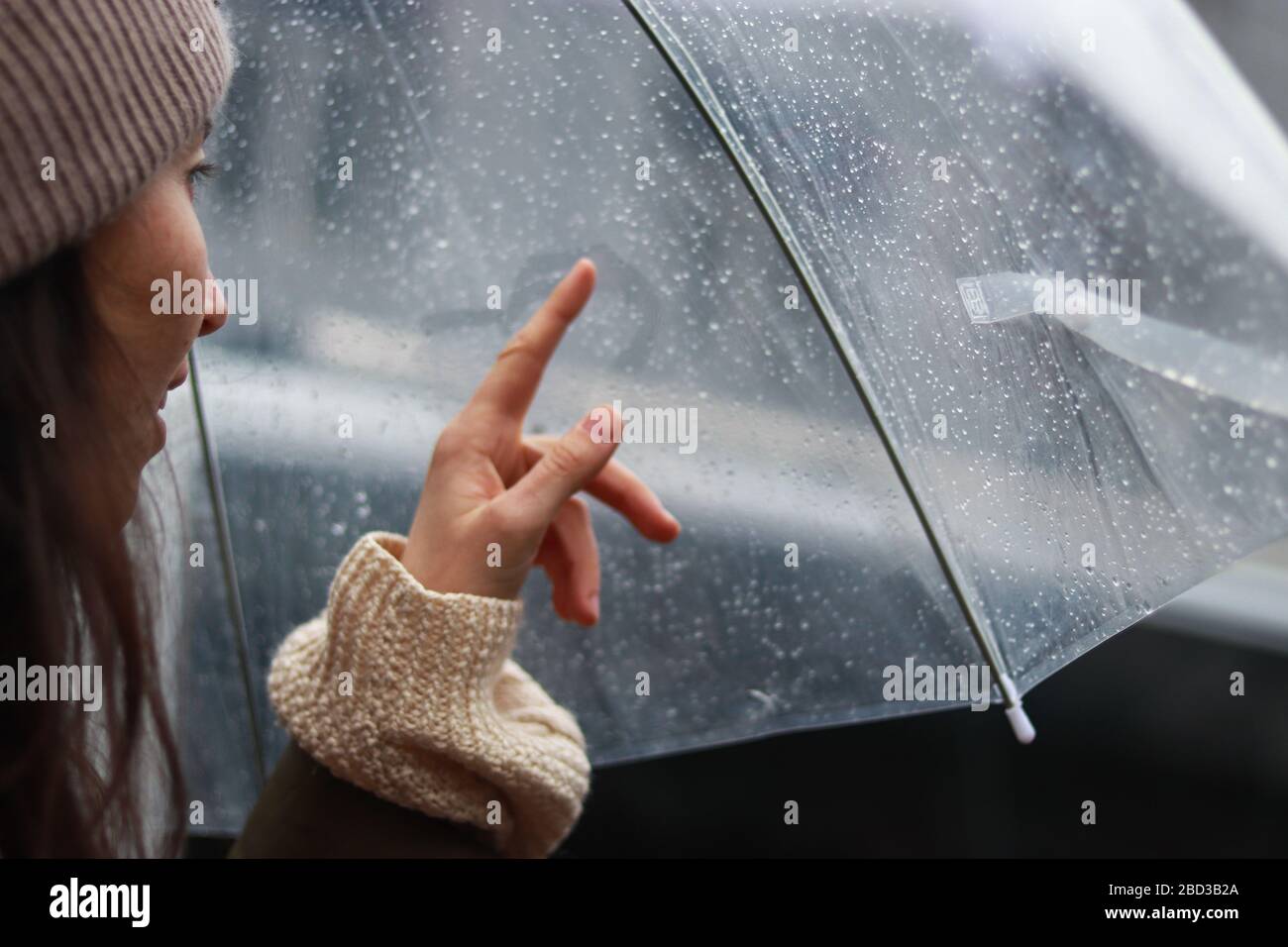 ragazza sta dipingendo il cuore su una superficie nebbiosa sotto la pioggia sotto un ombrello. Concetto di storia d'amore Foto Stock