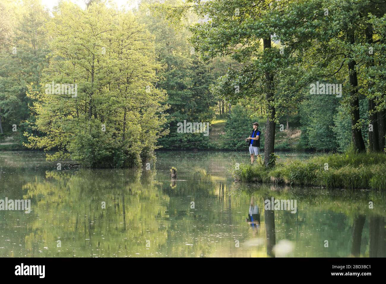 Uomo che pesca nel verde della natura selvaggia con la foresta lussureggiante in una giornata estiva soleggiata al tramonto. Foto Stock