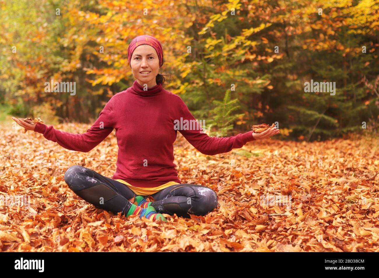 La ragazza in autunno siede sull'erba e getta allegramente le foglie gialle nella foresta. Stile di vita. Bella ragazza in verde foresta colorato all'aperto. Foto Stock