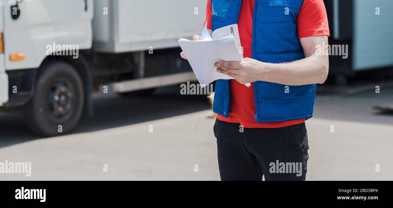 Corriere in uniforme prendendo appunti nel documento e consegna camion bianco lo behinde Foto Stock