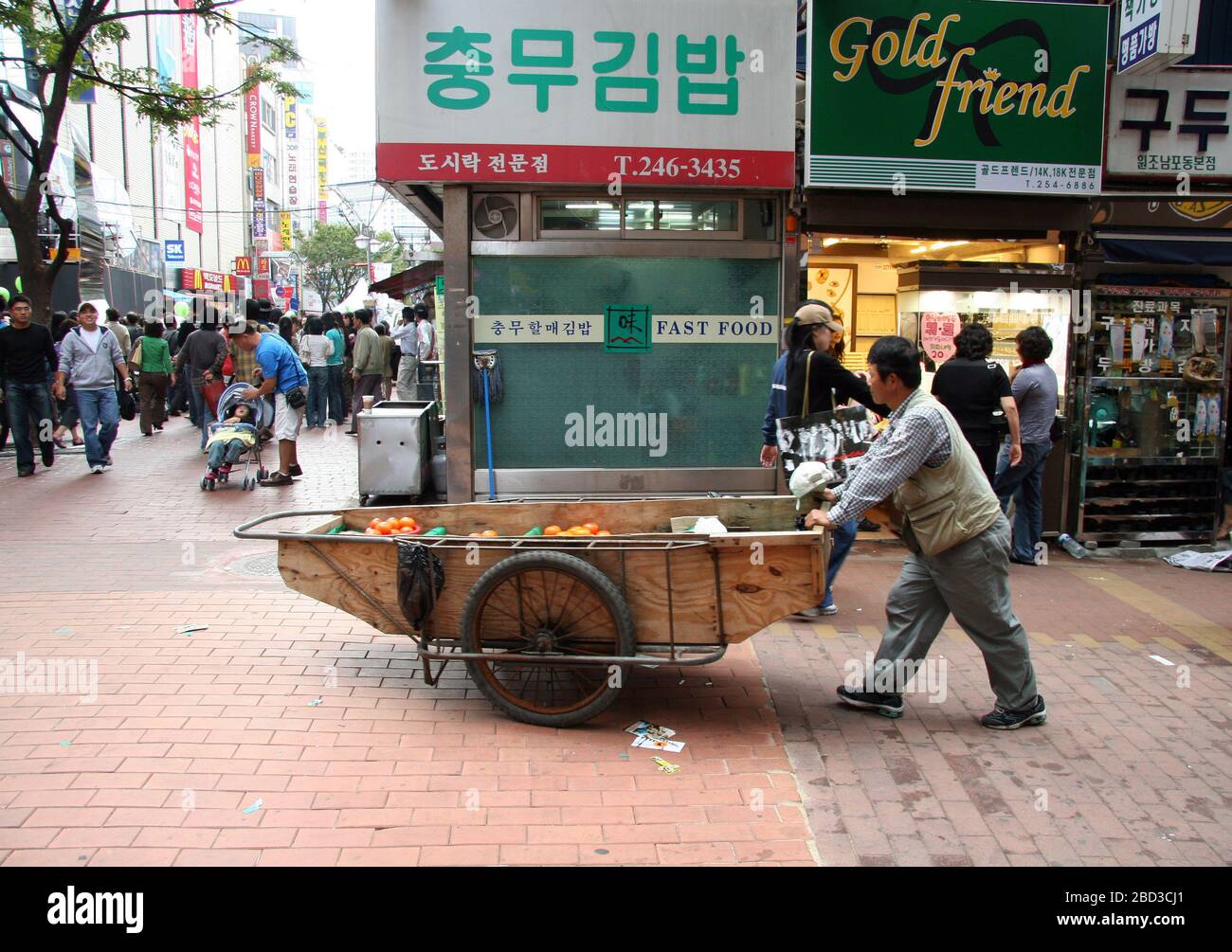 Un uomo spinge un carretto a ruote pieno di frutta attraverso le strade affollate di Busan, Corea del Sud Foto Stock