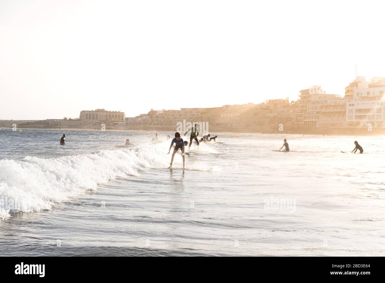 Vista posteriore di giovani surfisti che cavalcano una piccola onda al tramonto Foto Stock