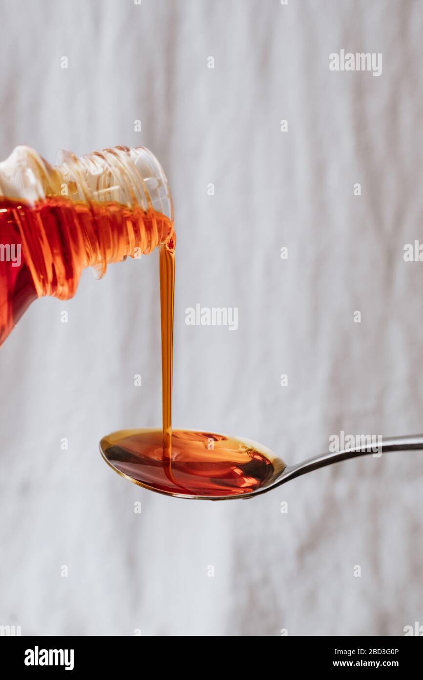 Medicinale liquido arancione brillante versato su un cucchiaino da tè metallico Foto Stock