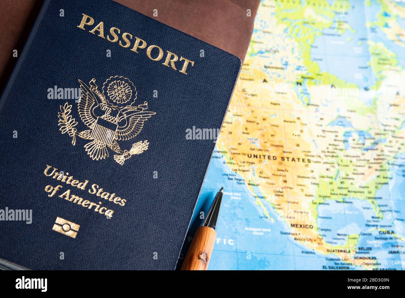 La copertina blu scuro stampata in foglio di un passaporto americano con notebook da viaggio rivestiti in pelle e penna per scrivere sullo sfondo di una mappa del mondo. Foto Stock