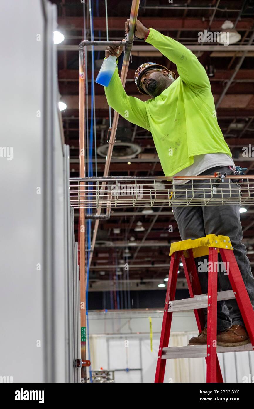 Detroit, Michigan, Stati Uniti. 6 Aprile 2020. I lavoratori costruiscono un ospedale di emergenza presso il centro congressi TCF. L'ospedale a 1,000 letti si occuperà dei pazienti con Covid-19. Un idraulico controlla l'eventuale presenza di perdite in una tubazione dell'ossigeno appena installata. Credit: Jim West/Alamy Live News Foto Stock