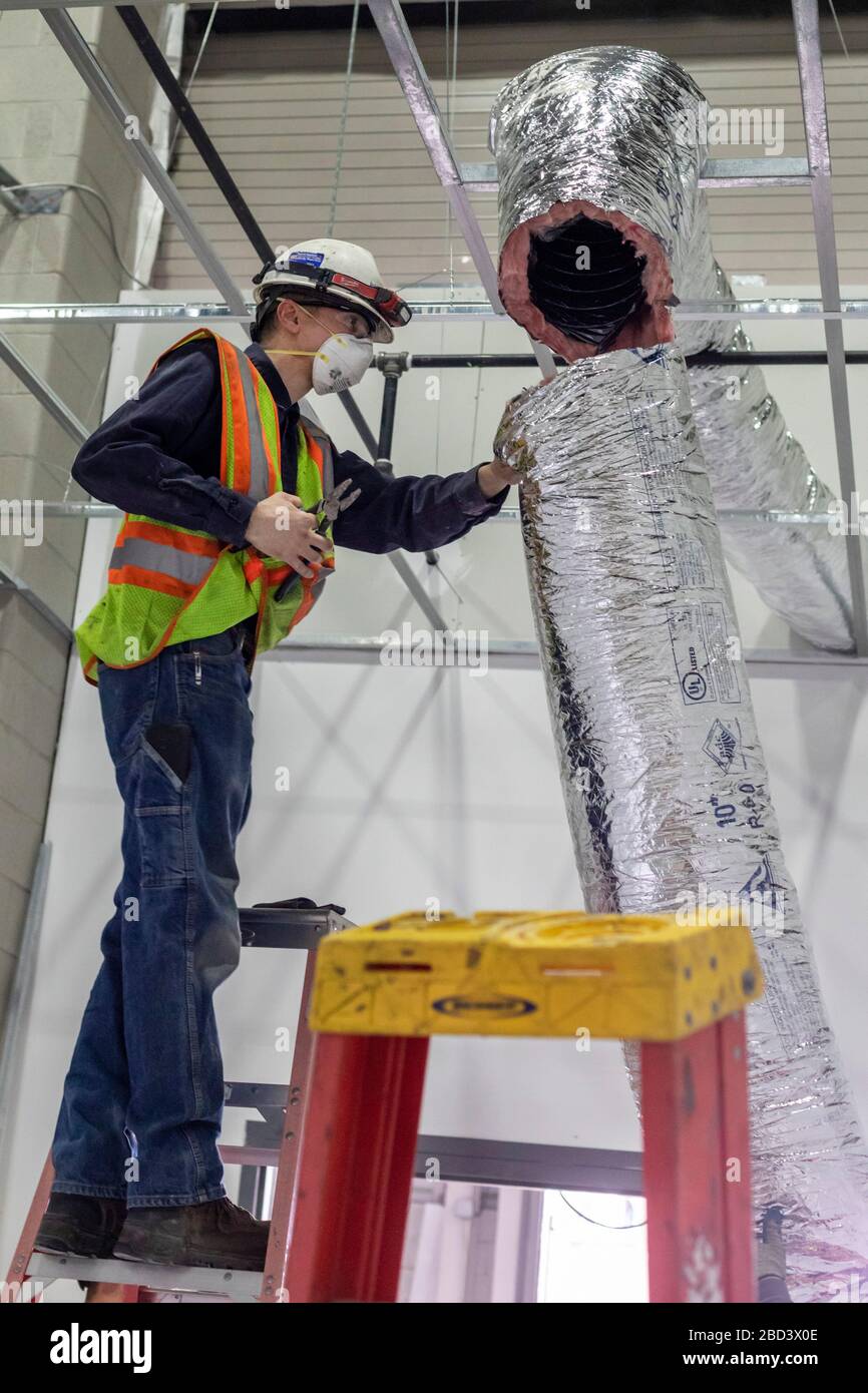 Detroit, Michigan, Stati Uniti. 6 Aprile 2020. I lavoratori costruiscono un ospedale di emergenza presso il centro congressi TCF. L'ospedale a 1,000 letti si occuperà dei pazienti con Covid-19. Un lavoratore installa le tubazioni di un sistema di pressione dell'aria negativa. Credit: Jim West/Alamy Live News Foto Stock