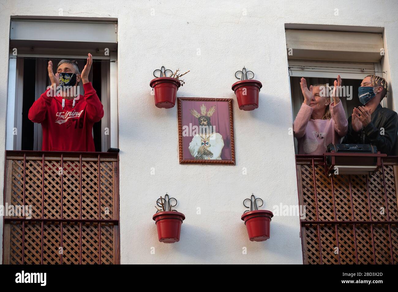 I credenti applauding sul loro balcone come mostrano gratitudine ai medici e infermieri durante un Lunedi Santo nel centro di Malaga.la tradizionale celebrazione di Pasqua è stato annullato in Spagna. I credenti vivono una settimana Santa inusuale nelle loro case, per questo motivo molte persone decorano i loro balconi con immagini di Cristo e della Vergine Maria. Dopo lo stato di allarme e il blocco nel paese da parte del coronavirus COVID-19, tutte le persone sono racchiuse nelle loro case in seguito al confinamento decretato dal governo spagnolo e che sarà prorogato per più di 15 giorni fino al 26 aprile. Foto Stock