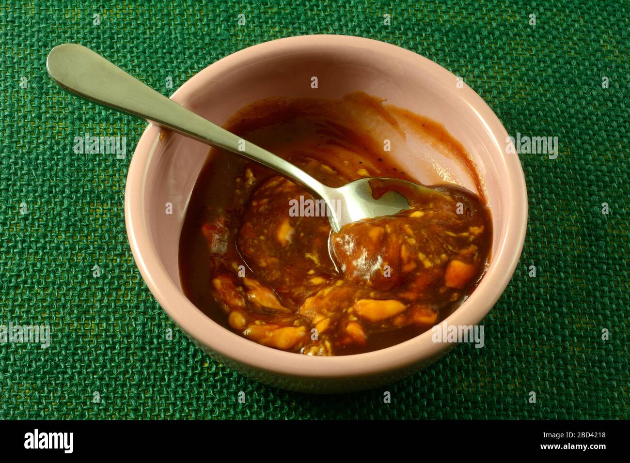 Mescolando la salsa al barbecue e le salse di chipotle aioli con il cucchiaio in una piccola ciotola di condimenti rosa Foto Stock