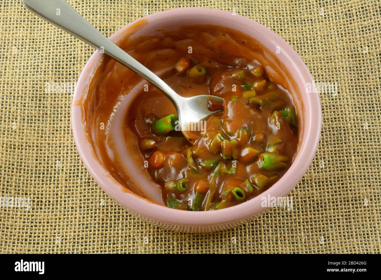 Aggiungere cipolle verdi tritate alla salsa al barbecue chipotle aoili con cucchiaio in una piccola ciotola per condimenti rosa Foto Stock