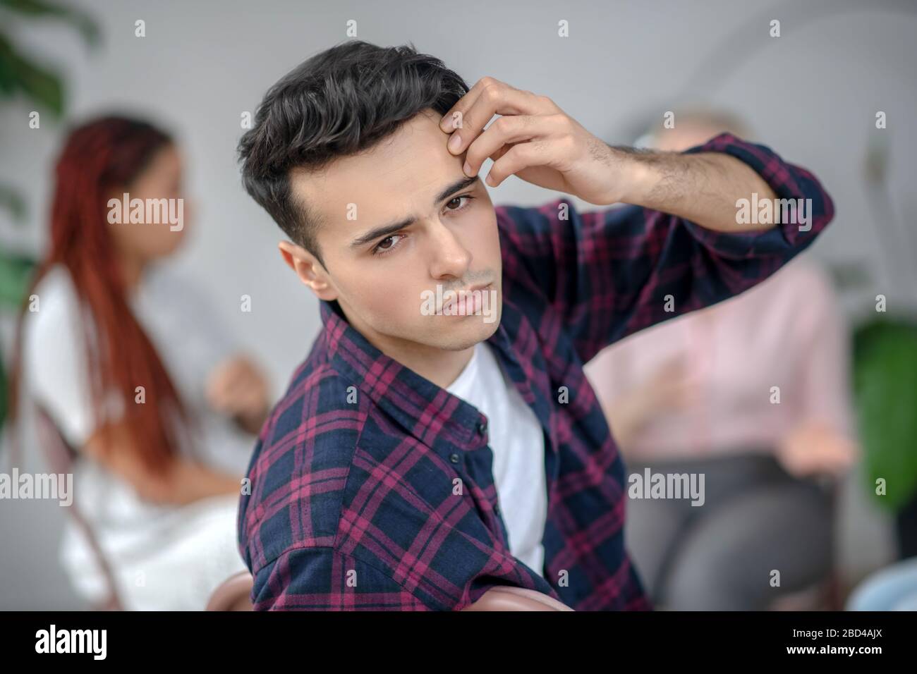Giovane uomo in camicia a scacchi che si sente male e tocca la testa Foto Stock