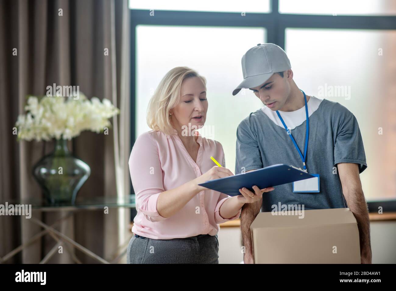 Donna bionda in una blusa rosa che incontra il corriere di consegna Foto Stock
