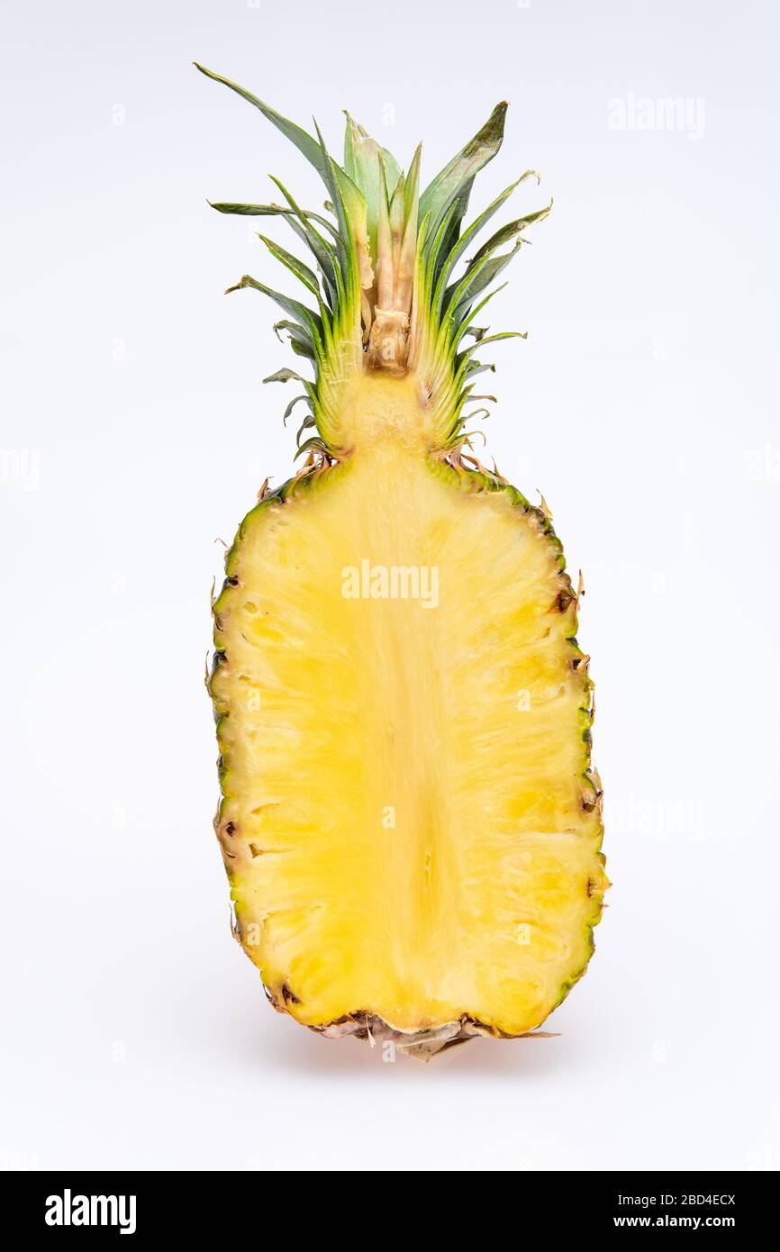 ananas tagliato a metà isolato di fronte a uno sfondo bianco. Il cuore giallo della frutta è succoso e colorato con foglie verdi Foto Stock